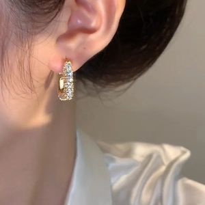 Elegant gold hoop earrings with square cubic zirconia stones worn on a model's ear