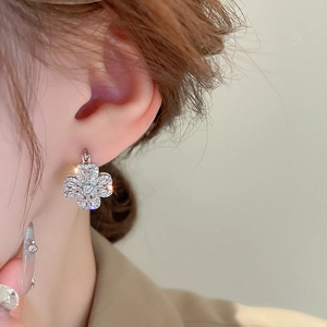 Macro shot of silver four-leaf clover earring with sparkling cubic zirconia on ear