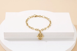 Golden Hamsa Hand bracelet on white geometric pedestal with a polished link chain