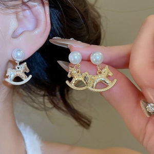 Detail of elegant rocking horse earrings with pearls worn by a model in soft light