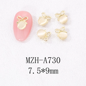 Détail de charmes pour ongles noeud doré 7,5x9mm avec perles œil de chat sur manucure rose