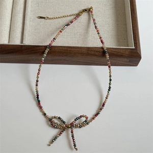 Close-up of beaded necklace with woven bow pendant and adjustable gold chain