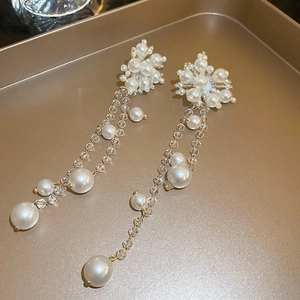 Detailed close-up of elegant long pearl tassel earrings with gold finish on a tray