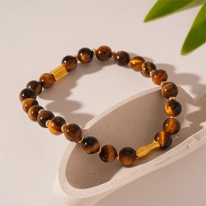 Macro detail of tiger eye beaded bracelet with golden peanut charm on ceramic decor