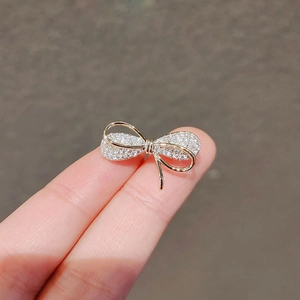 Close-up of a small gold bow brooch with pavé crystals held between fingers