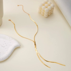Elegant gold flat snake bone tassel necklace layered on a cream minimalist background