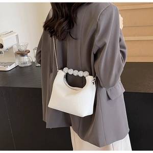 Close-up of white pebble leather dumpling bag with elegant pearl handle and metal chain