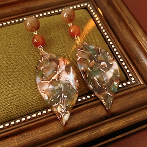 Detailed view of retro acetate leaf earrings with amber beads on a green fabric backdrop