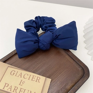 Detail view of navy blue satin bow scrunchie on a dark wooden tray in elegant setting