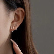 Macro shot of hollow cat-shaped silver earrings on ear showing delicate design