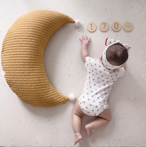 Quilted cotton moon-shaped nursing pillow in ginger with white pompoms for infants