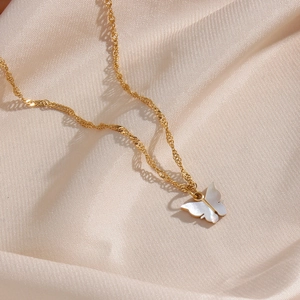 Close-up of golden butterfly necklace with white shell inlay on beige silk fabric
