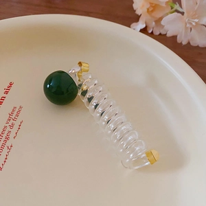 Detailed close-up of a sweet dopamine transparent spiral hair tie with a dark green bead and gold ends.