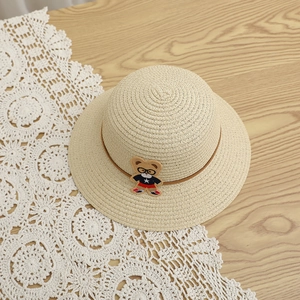 Children's straw sun hat with cute bear applique and brown ribbon on wooden background