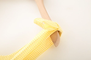 Detail of yellow and white gingham strap dress with bow tie design on a wooden hanger