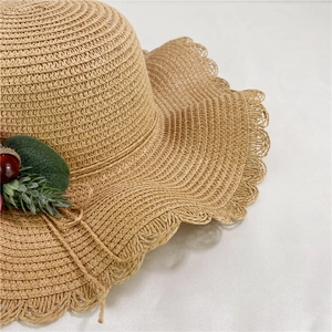 Détail d'un chapeau de paille à bord festonné avec feuille verte et baies rouges