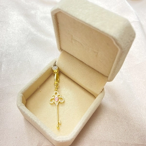 Détail d'un clip de nombril clé dorée avec gemme de cœur rose dans un coffret à bijoux