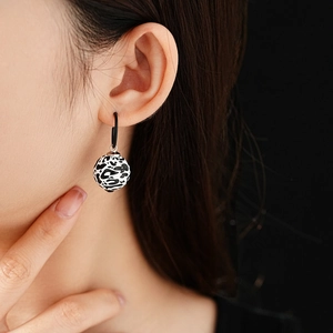 Close-up of black and white leopard print ball earrings on a model with black studs