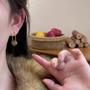 Detailed side view of a gold spherical pendant earring worn by a model in warm light