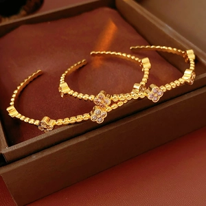 Dettaglio di braccialetti a quadrifoglio placcati oro 18k con zirconi su portagioie in pelle