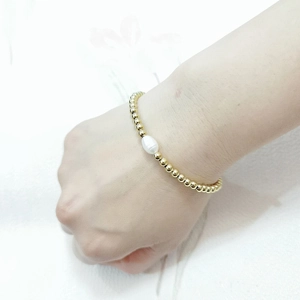 Detail of 4mm gold beaded bracelet featuring a freshwater pearl on a female wrist