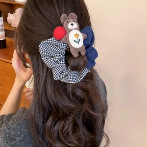 Detail of fabric bow hair tie with blue plaid pattern and cute plush bear accessory