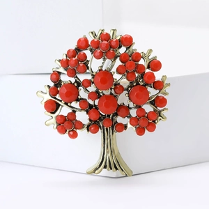 Detailed view of a golden tree of life brooch with red rhinestones on white stands