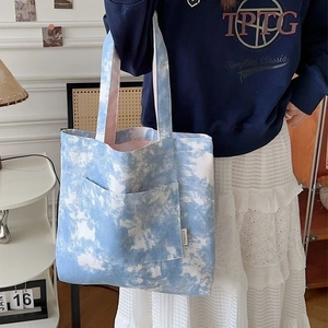 Borsa tote in tela tie-dye blu e bianca con tasca frontale indossata a spalla