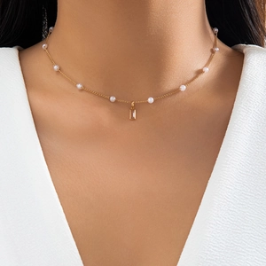 Detail of gold chain necklace featuring white pearls and a clear rectangular gemstone
