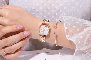Gros plan d'une montre carrée en or rose pour femme avec cadran en nacre au poignet
