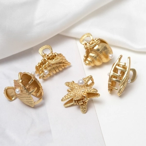 Elegant gold shell and starfish hair clips with pearls displayed on white silk and marble