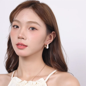 Close-up of minimalist C-shape gold earring with white pearl stud on female model ear