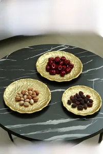Detail of round golden iron tray with wavy texture and nuts on marble background