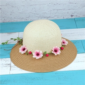 Detail of a straw sun hat featuring a beige crown and light brown brim with floral wreath