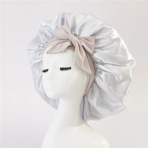 Detail of silver satin sleep bonnet with a large beige bow for hair protection