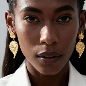 Close-up of a model wearing textured gold-tone leaf-shaped earrings with metallic finish