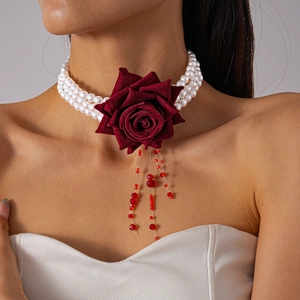 Détail du tour de cou en perles à trois couches avec rose en velours rouge et pompons