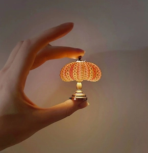 Miniature vintage urchin lamp held between fingers showing tiny scale and warm light