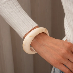 Gros plan sur le bracelet jonc large en résine marbrée crème à la texture lisse