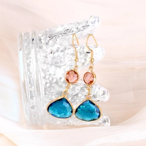 Detailed macro of gold drop earrings featuring blue faceted crystals and orange round stones