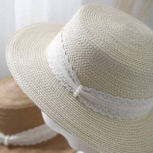 Close-up of beige straw hat featuring delicate lace ribbon and elegant pearl details