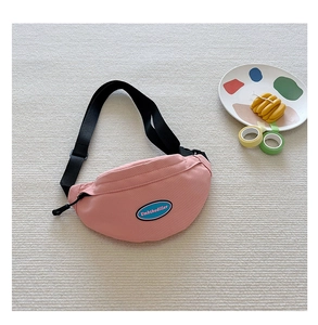 Detail of pink canvas chest bag featuring a blue logo patch and adjustable black strap
