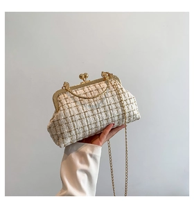Detail of beige tweed handbag featuring gold metallic threads and curved metal handle