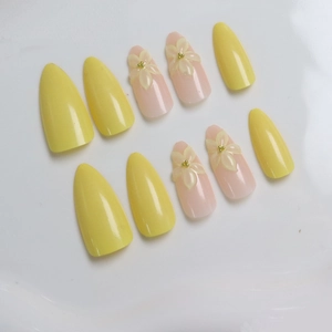 Detail of almond-shaped press-on nails with 3D yellow flowers and gold bead accents