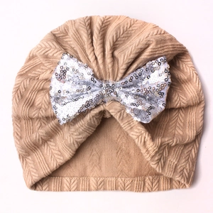 Detailed close-up of a beige baby knit hat featuring a shimmering silver sequin bow