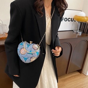 Detail of blue heart-shaped sequin clutch bag with floral embroidery and gold handle