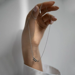 Detail view of a 925 sterling silver leaf pendant bracelet held by hand on a grey background