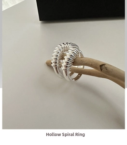 Macro de un anillo de plata S925 con diseño de espiral hueca colgado en una rama de madera