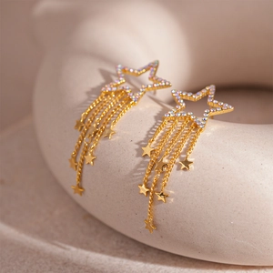 Macro detail of elegant gold star tassel earrings with zircon inlay on a ceramic stand
