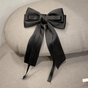 Close-up of black satin bow hair clip with long flowing ribbons and soft silky texture